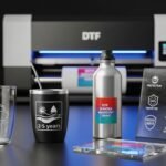 Imagem realista de itens personalizados com impressão DTF UV — caneca de vidro, copo, squeeze de alumínio e placa de acrílico — com adesivos em leve relevo e acabamento brilhante. As estampas destacam durabilidade e resistência, com ícones de proteção UV, água e riscos, em um ambiente profissional com impressora UV ao fundo.
